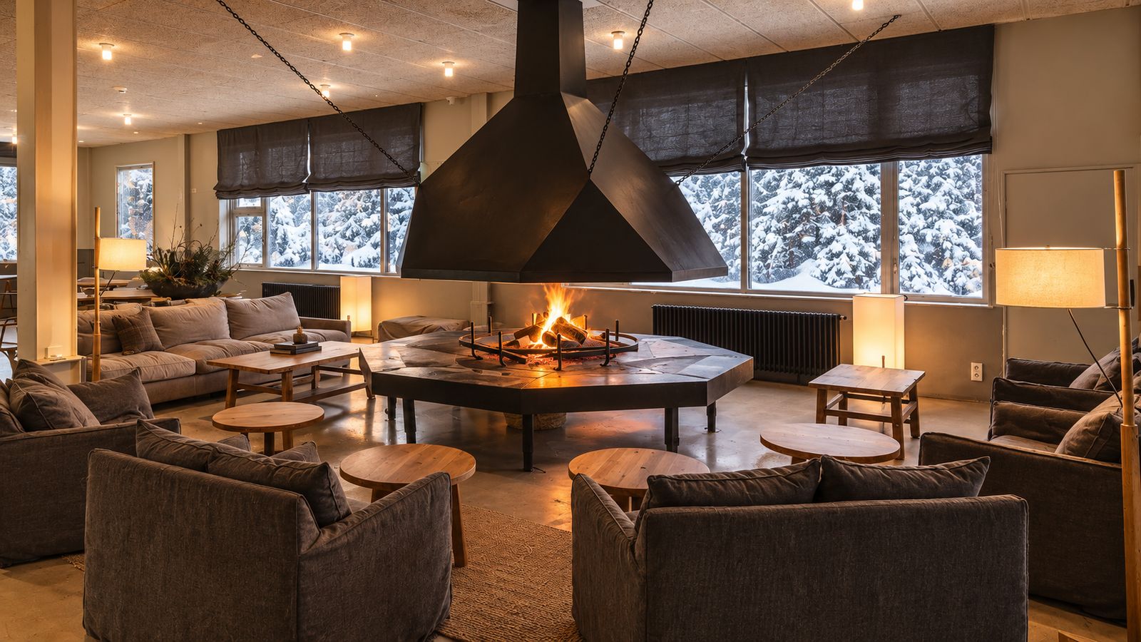 Salón del hotel con la chimenea central y vistas a los pinos nevados